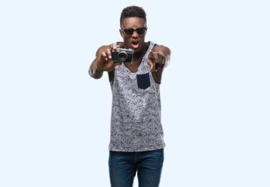 Genç Afro-Amerikan adam holding vintage fotoğraf makinesi kamera ve size, el işareti, pozitif ve kendinden emin bir jest ön parmak ile işaret