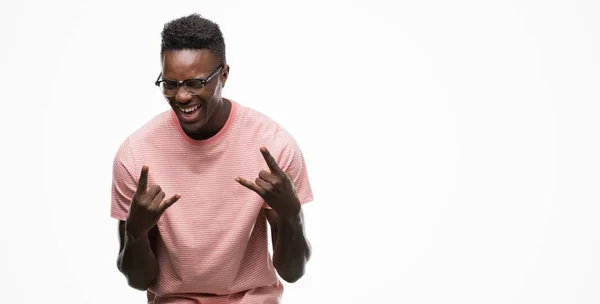 年轻的非洲裔美国人穿着粉红色 T恤大喊着疯狂的表情做摇滚符号用手 音乐明星 重的概念 — 图库照片