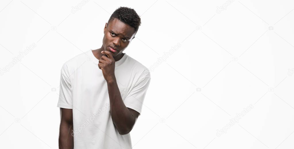 Young african american man wearing white t-shirt with hand on chin thinking about question, pensive expression. Smiling with thoughtful face. Doubt concept.