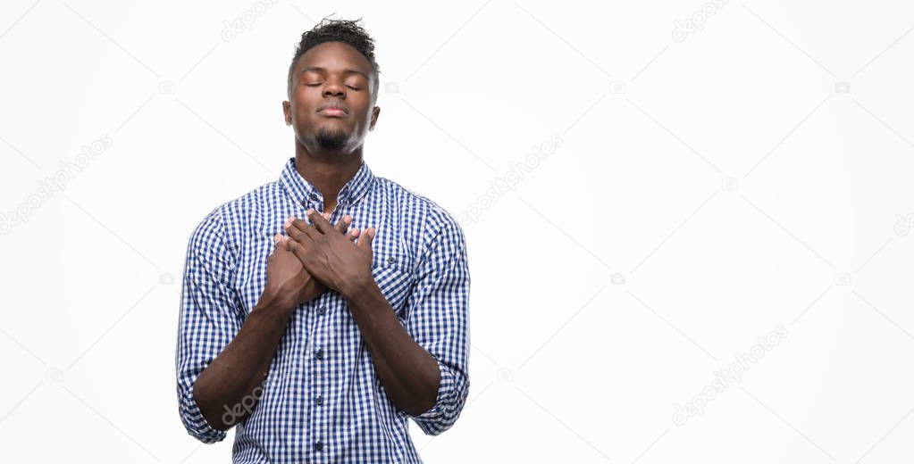Young african american man wearing blue shirt smiling with hands on chest with closed eyes and grateful gesture on face. Health concept.