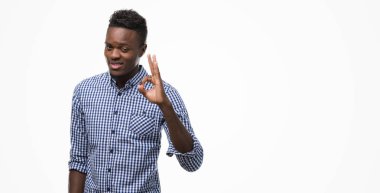El ve parmak ile ok işareti yapıyor olumlu gülümseyen mavi gömlek giymiş genç Afro-Amerikan adam. Başarılı ifade.