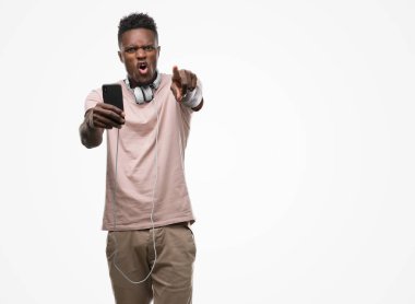 Genç Afro-Amerikan adam giyen kulaklık ve kamera ve size parmak ile işaret holding smartphone, el işareti, pozitif ve kendinden emin bir jest ön