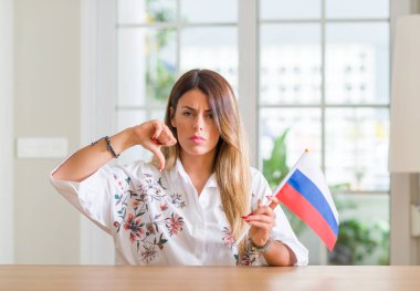 Young woman at home holding flag of Russia with angry face, negative sign showing dislike with thumbs down, rejection concept clipart