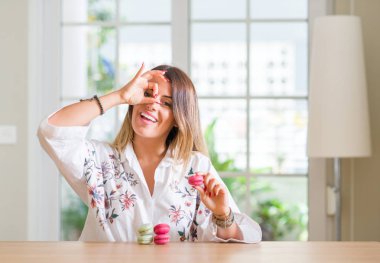 Mutlu yüz el parmaklarının arasından seyir göz üzerinde ok işaretiyle yapıyor gülümseyen macarons genç kadın evde yemek