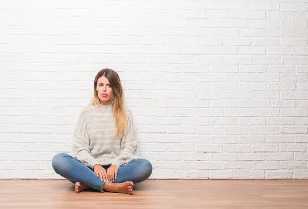 若い大人の女性が床に座って白いレンガの壁を自宅に懐疑論者と神経 しかめっ面の動揺の問題のため 否定的な人 — ストック写真