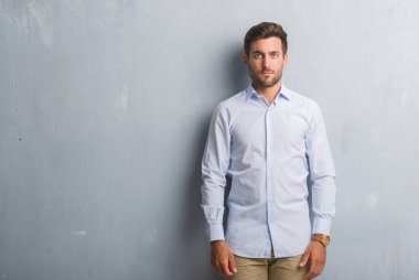 Yakışıklı genç iş adamı yüzünde ciddi bir ifade ile şık gömlek giymiş gri grunge duvarın üzerinden. Basit ve doğal kameraya bakıyor.