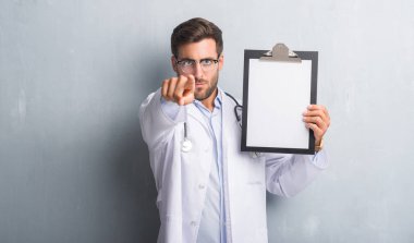 Parmak ile işaret kamera ve size, el işareti, pozitif ve kendinden emin bir jest ön Pano tutan gri grunge duvarın üzerinden adam yakışıklı genç doktor