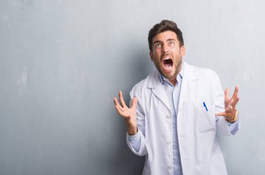 Yakışıklı genç profesyonel adam beyaz giyen gri grunge duvarın üzerinden kat çılgın ve kızgın bağırarak ve agresif ifade ve silah kaldırdı bağırıyordu. Hayal kırıklığı kavramı.