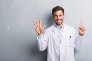 Profesyonel yakışıklı genç gösterilen ve parmakları ile işaret beyaz önlük giyen gri grunge duvarın üzerinden 6 kendinden emin ve mutlu gülümseyerek iken numara.