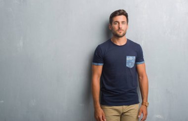 Yakışıklı genç gri grunge duvarın yüzünde ciddi bir ifade ile üzerinden. Basit ve doğal kameraya bakıyor.