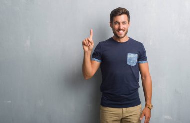 Yakışıklı delikanlı gösterilen ve parmak gülümseyen süre bir numara ile kendinden emin ve mutlu yukarıyı gri grunge duvarın üzerinden.