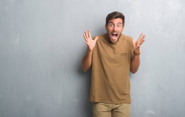 Yakışıklı genç gri grunge üzerinde kutluyor deli duvar ve çığlık kaldırdı ve açık gözleri hayret silah ile başarı için heyecanlı. Kazanan kavramı