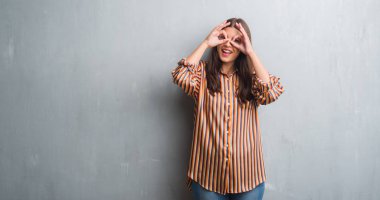 Genç esmer kadın dilini, parmaklarının arasından baktığını yapışmasını dürbün gibi ok jest yapıyor grunge gri duvar yüzünden. Deli ifade.