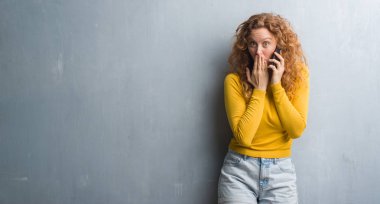 Hata, korku, sessizlik içinde gizli kavramı korkmuş ifade için utanç ile genç Kızıl saçlı kadın telefon kapağı ağız el ile konuşurken gri grunge duvarın üzerinden şok
