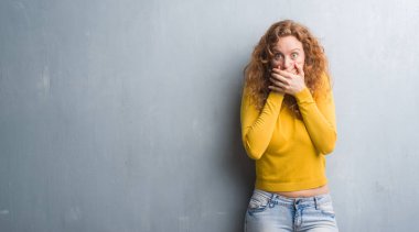 Genç Kızıl saçlı kadın gri grunge duvar eller için hata ile ağız kapsayan şok yüzünden. Gizli kavramı.
