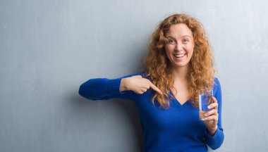 Gri grunge duvar içme suyu sürpriz yüz işaret parmağı kendine genç Kızıl saçlı kadın