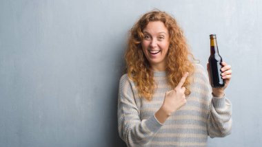 Gri grunge duvar bira şişesi çok mutlu el ve parmak ile işaret tutan genç Kızıl saçlı kadın