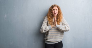 Yalvarıyor ve umut ifade yüzünde çok duygusal ve endişe ile birlikte elleriyle dua gri grunge duvarın üzerinden genç Kızıl saçlı kadın. Bağışlanmak. Din kavramı.