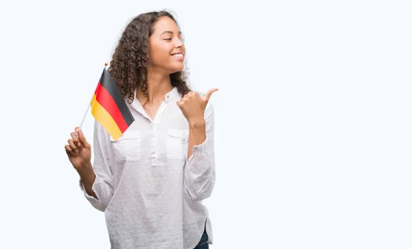 年轻的西班牙裔妇女持有德国国旗指着和显示与拇指的一面微笑着快乐的脸 — 图库照片
