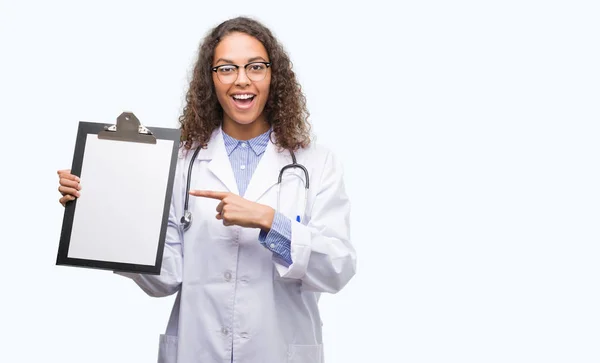 Joven Doctora Hispana Sosteniendo Portapapeles Muy Feliz Señalando Con Mano —  Fotos de Stock