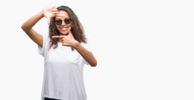 Genç İspanyol kadın elle yapma çerçeve ve parmakları ile mutlu yüz gülümseyen güneş gözlüğü takıyor. Yaratıcılık ve Fotoğrafçılık kavramı.