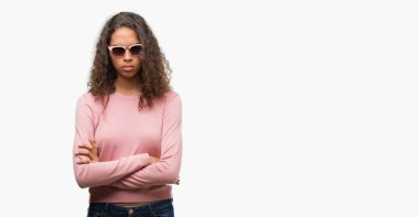 Çapraz kolları olan yüzündeki güneş gözlüğü şüpheci ve sinir, onaylamayan ifade giyen güzel genç İspanyol kadın. Negatif kişi.