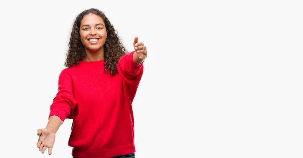 ハグするため両手を広げて笑みを浮かべてカメラを見て赤いセーターを着ている若いヒスパニックの女性 晴れやかな表情の受け入れ幸せ — ストック写真