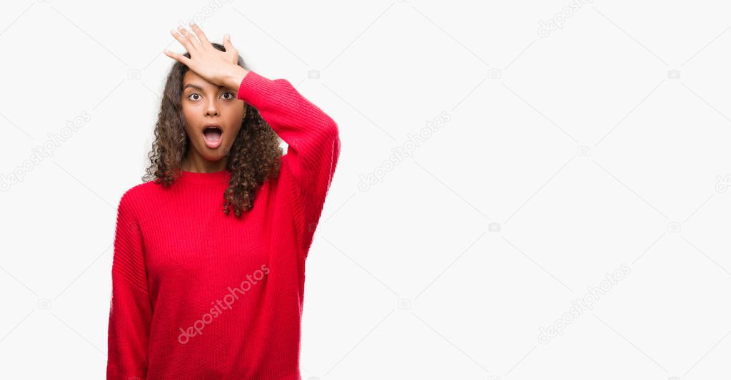 Young hispanic woman wearing red sweater surprised with hand on head for mistake, remember error. Forgot, bad memory concept.