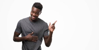 Kameraya bakarak yan el ve parmak ile işaret, yüzünde kocaman bir gülümseme ile gri t-shirt giyen genç Afro-Amerikan adam.