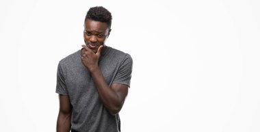 Emin çapraz kollar ve çeneme kaldırdı el ile gülümseme ile kamera seyir gri t-shirt giyen genç Afro-Amerikan adam. Pozitif düşünce.