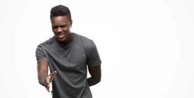 Tebrik ve konuksever dost sunan karşılıklı gülümseyen gri t-shirt giyen genç Afro-Amerikan adam. Başarılı iş.