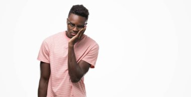 Pembe tişört düşünme seyir giyen genç Afro-Amerikan adam yorgun ve sıkılmış çapraz silah depresyon sorunları ile.