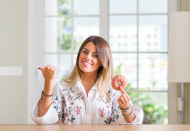 Genç kadının evde el ve parmak ile yukarı dönük mutlu yüz gülümseyen ile bir çörek yediğini