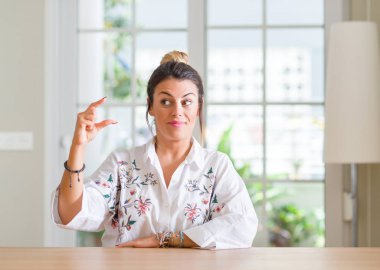 Genç kadın evde gülümseyen ve kendine güvenen boyutu işaret parmaklı ararken ve kamera işi el ile el hareketi. Ölçü kavramı.