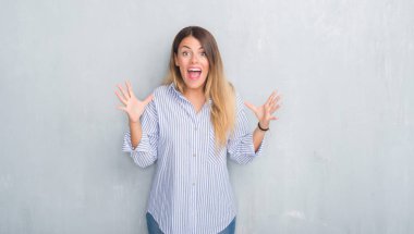 Gri grunge Genç Yetişkin kadın duvar giyen moda iş kıyafeti deli ve çığlık kaldırdı ve açık gözleri heyecanlı silah ile başarı için hayran kutluyor. Kazanan kavramı