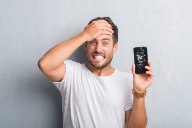Kırık smartphone ekran başında, el ile vurguladı gösterilen gri grunge duvarın üzerinden yakışıklı genç adam şok utanç ve sürpriz suratla, öfkeli ve sinirli. Korku ve hata için üzgün.