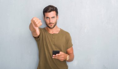 Gri grunge yakışıklı genç adam kızgın yüz ile smartphone kullanarak bir ileti manifatura duvar, sevmediğim başparmak aşağı, ret kavramı ile gösterilen işareti negatif