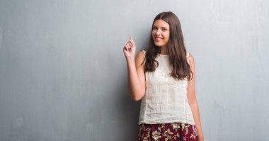 Grunge genç esmer kadın duvar bir fikirle sürpriz gri veya gülen yüz, bir numara ile işaret parmağı soru