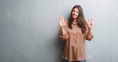 Genç esmer kadın gösterilen ve parmakları ile işaret grunge gri duvar yüzünden kendinden emin ve mutlu gülümseyerek süre sekiz numara.