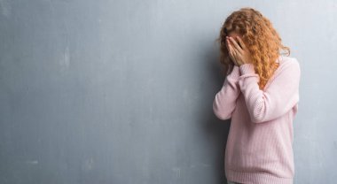 Genç redhead gri grunge duvar giyen üzerinde pembe kadın kazak üzgün ifadeyle yüz eller ile ağlayarak süre kapsayan. Depresyon kavramı.