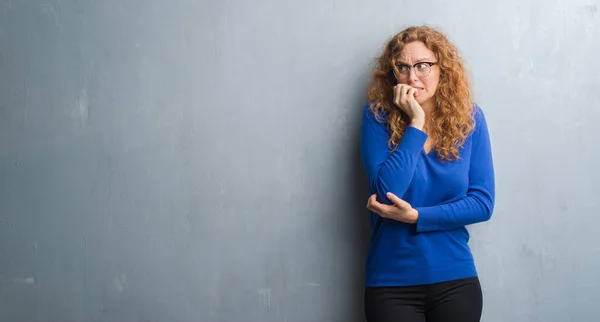 灰色垃圾墙上的年轻红头发的女人看着压力和紧张的嘴咬指甲的手 焦虑问题 — 图库照片