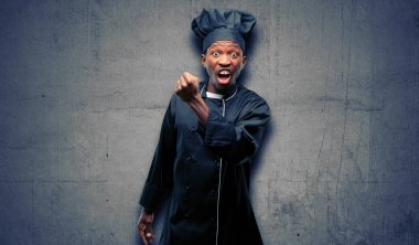 Genç siyah giyen chef şapka sinirli ve öfkeli olumsuz duygu, biriyle rahatsız ifade yemek