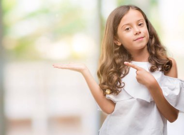 Hayret ve el ile sunulması ve parmak ile işaret ederken kameraya gülümseyen esmer Latin kız.