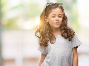 Esmer Latin kız giyiyor güneş gözlüğü seksi bir ifadeyle, neşeli ve mutlu yüzünü kameraya bakarak göz kırpıyor.