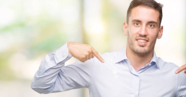 Yüzünde gülümseme ile kendinden emin görünüyorsun, kendini gururlu ve mutlu parmakları ile işaret yakışıklı genç işadamı.