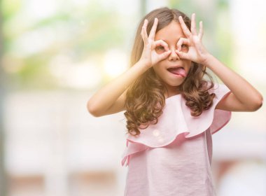 Esmer Latin kız dilini, parmaklarının arasından baktığını yapışmasını dürbün gibi ok jest yapıyor pembe elbise. Deli ifade.