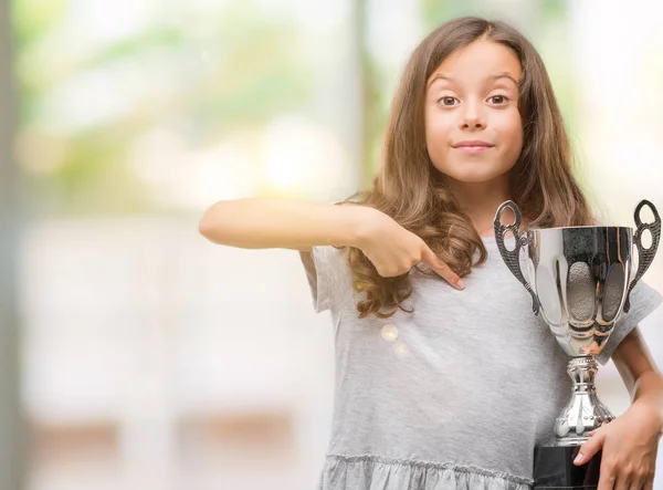 Brunette Hispanic Girl Holding Trophy Surprise Face Pointing Finger Himself — Stock Photo, Image