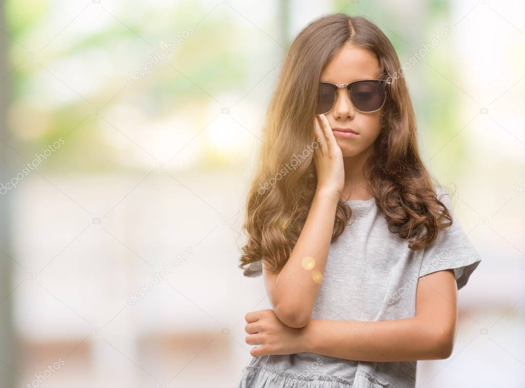 Brunette hispanic girl wearing sunglasses thinking looking tired and bored with depression problems with crossed arms.