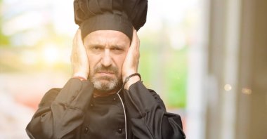 Üst düzey aşçı adam, aşçı şapkası kulakları rahatsız edici gürültü, görmezden kapsayan kulak işitme ses önlemek için fişler. Gürültülü müzik bir sorundur.