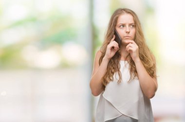 Genç Sarışın kadın Smartphone ciddi bir yüz düşünme soru hakkında çok kullanarak fikir karışık